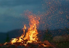 تصویر فوتیج آتش در هنگام غروب در پس زمینه کوه و جنگل 