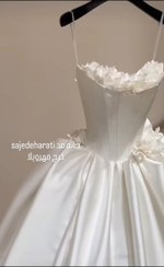 تصویر لباس عروس ساتن سفید یقه لباس دکلته تماما گن دوزی شده فنر کشی شده ، کار دست گل کار شده دامن این لباس پیله خورده اسکارلت هست مناسب سایز 36تا 38 